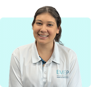A woman with dark hair tied back is smiling and wearing a white collared shirt with the logo EMEP on it, sitting against a light blue background.
