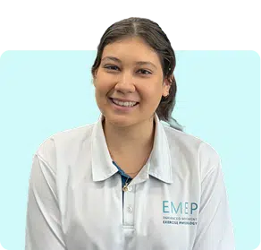 A woman with dark hair tied back is smiling and wearing a white collared shirt with the logo EMEP on it, sitting against a light blue background.