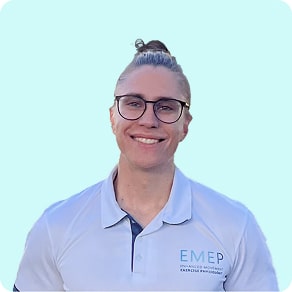 A person with long hair tied in a bun, wearing glasses and a light blue collared shirt with an EMEP logo, smiling against a light blue background.